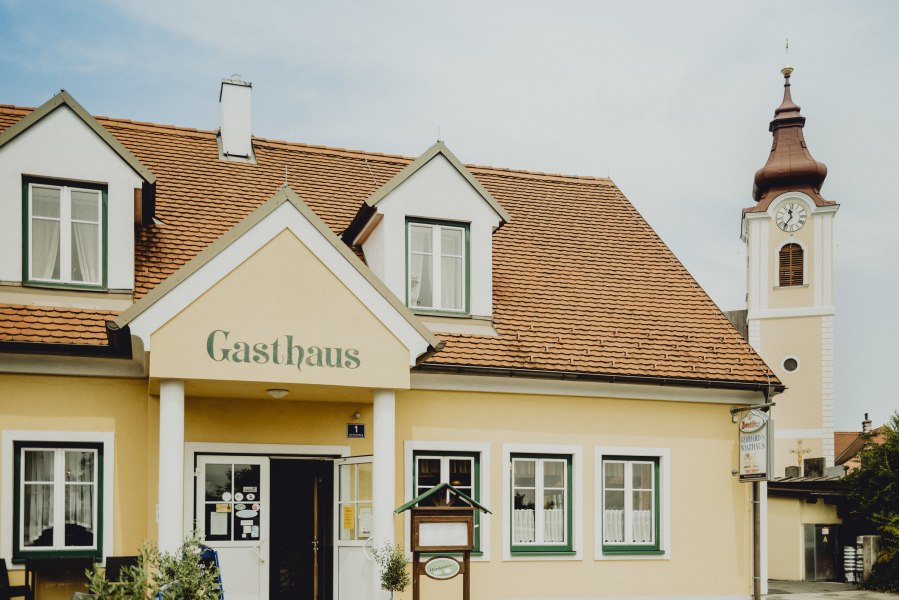 Ein gelbes Gasthaus mit roten Dachziegeln und einem Kirchturm im Hintergrund.