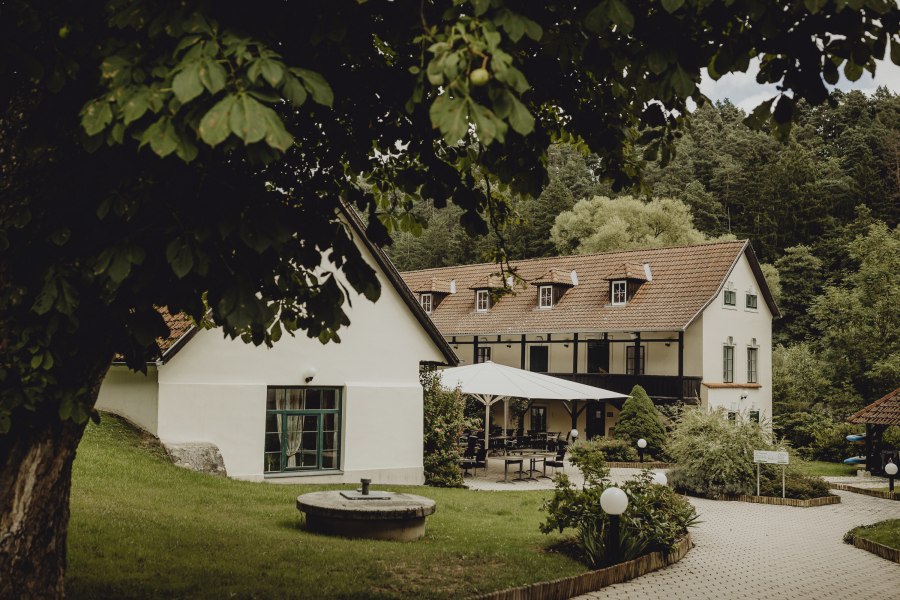 Ein idyllisches Wirtshaus mit Terrasse und Garten, umgeben von B&auml;umen.