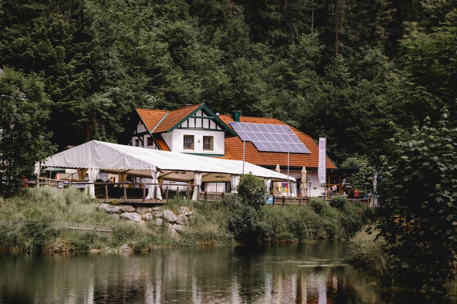 Gasthaus mit Solarpanelen und Zelt am Waldrand, nahe einem Teich.