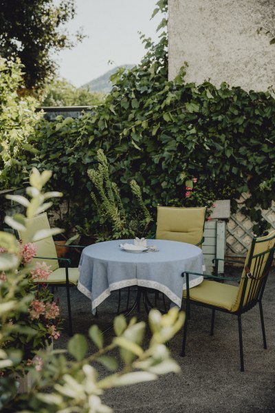 Ein runder Tisch mit blauer Tischdecke und vier St&uuml;hlen in einem gr&uuml;nen Garten.