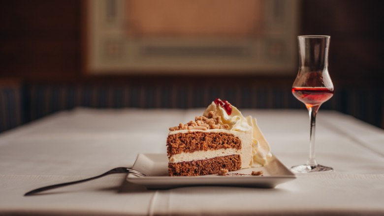 Ein St&uuml;ck Torte mit Sahne und ein Glas Lik&ouml;r auf einem gedeckten Tisch.