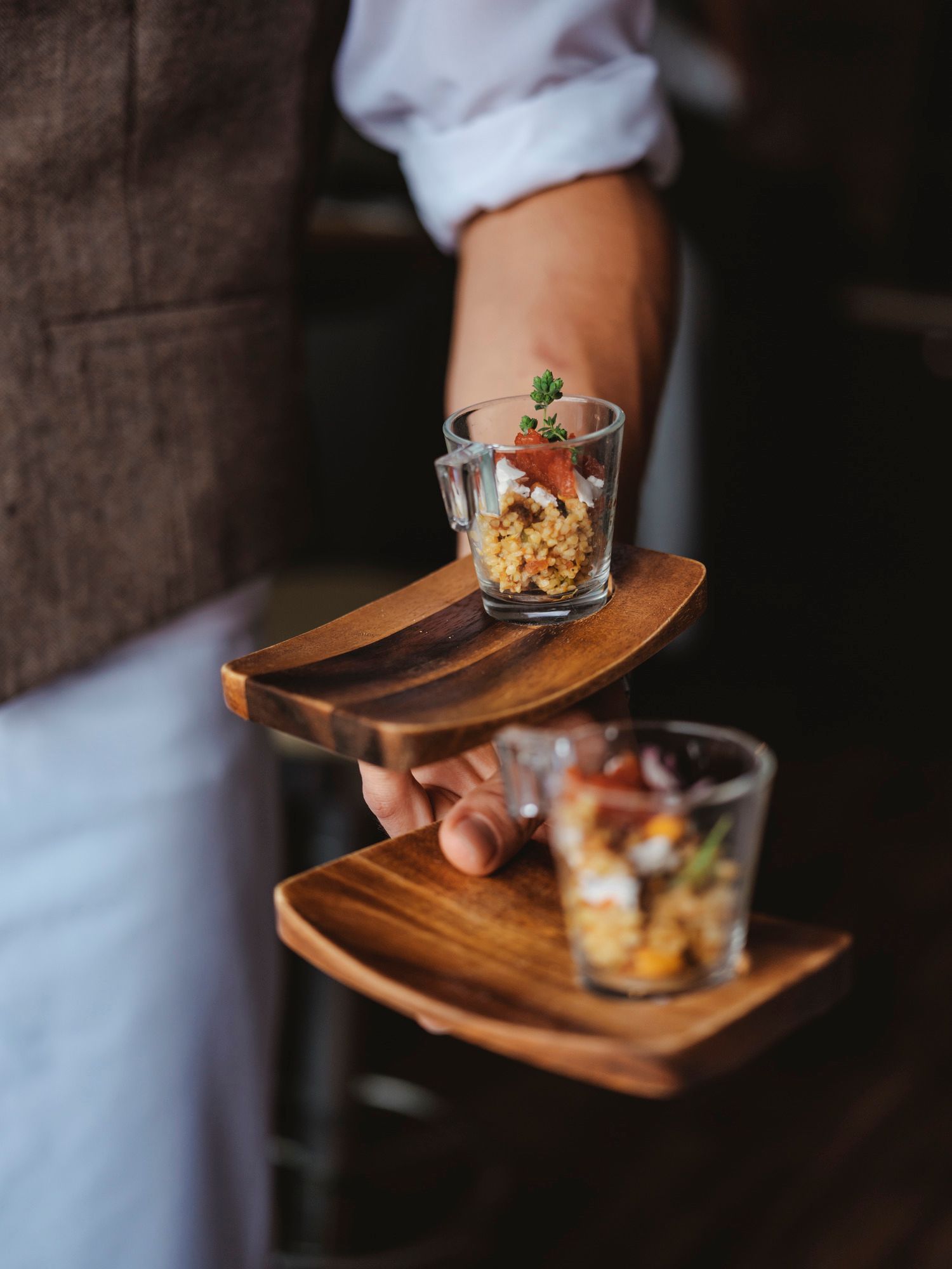 Ein Kellner serviert kleine Gläser mit Speisen auf Holztabletts.
