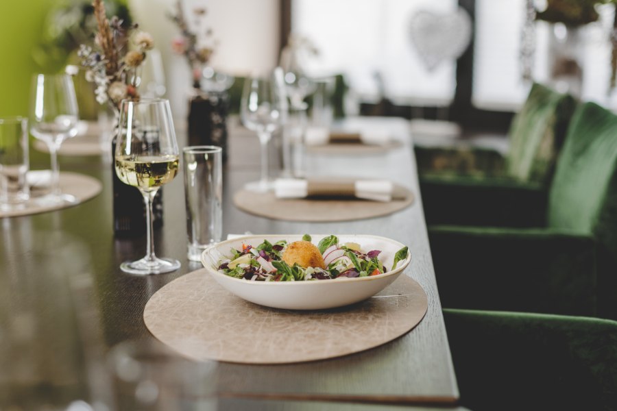 Ein gedeckter Tisch mit einem Salatteller und einem Glas Wei&szlig;wein.