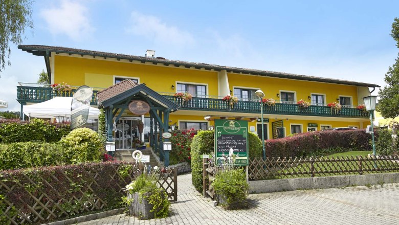 Gelbes Gebäude mit Balkon und Blumen, Krumbacherhof, Eingang mit Vordach und Schildern.