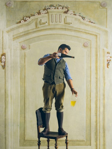 Hartmuth Rameder steht auf einem Stuhl und gie&szlig;t Wein  aus einer Flasche in ein Glas.