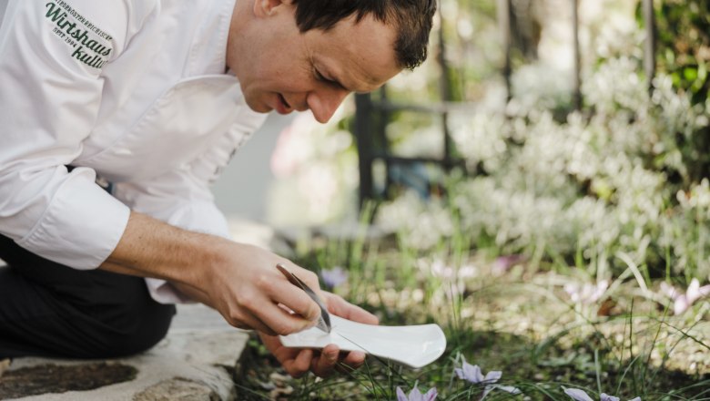 Der Koch Roman Siebenhandl kniet im Garten und erntet Safran mit einer Pinzette.