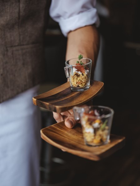 Ein Kellner serviert kleine Gl&auml;ser mit Speisen auf Holztabletts.
