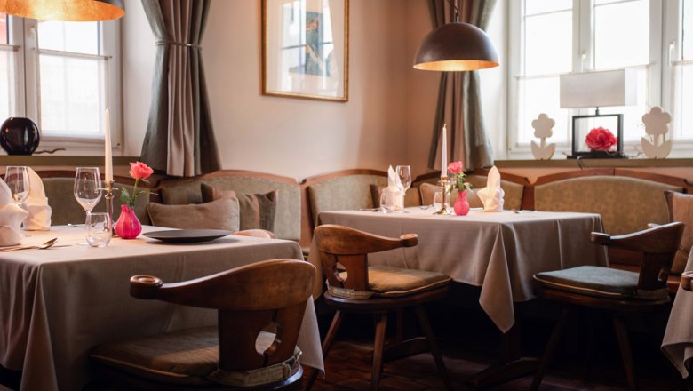Gem&uuml;tliche Gaststube mit gedeckten Tischen, Kerzen und Blumen in Pastellt&ouml;nen dekoriert.