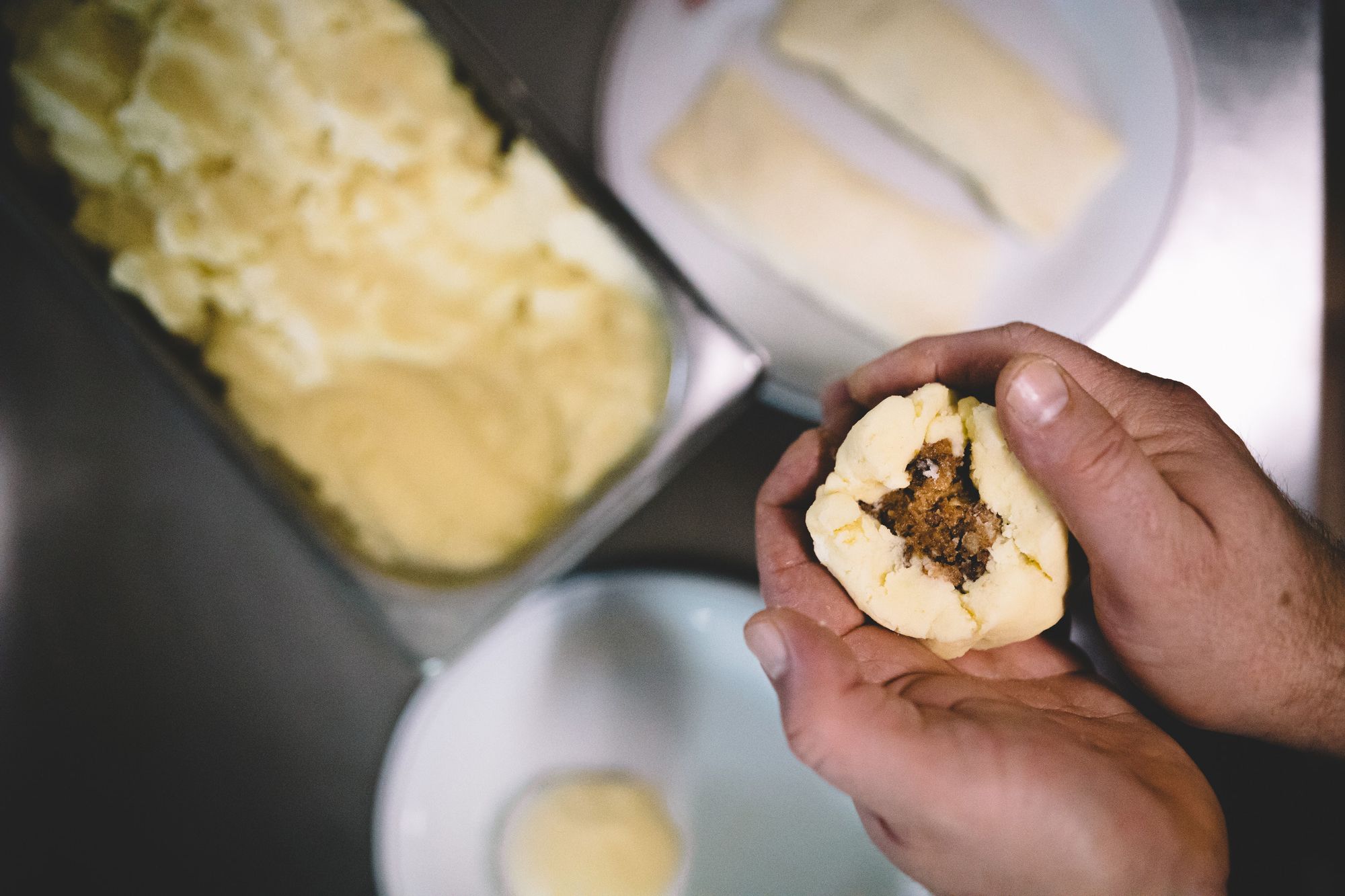 Hände formen einen gefüllten Knödel aus Teig.