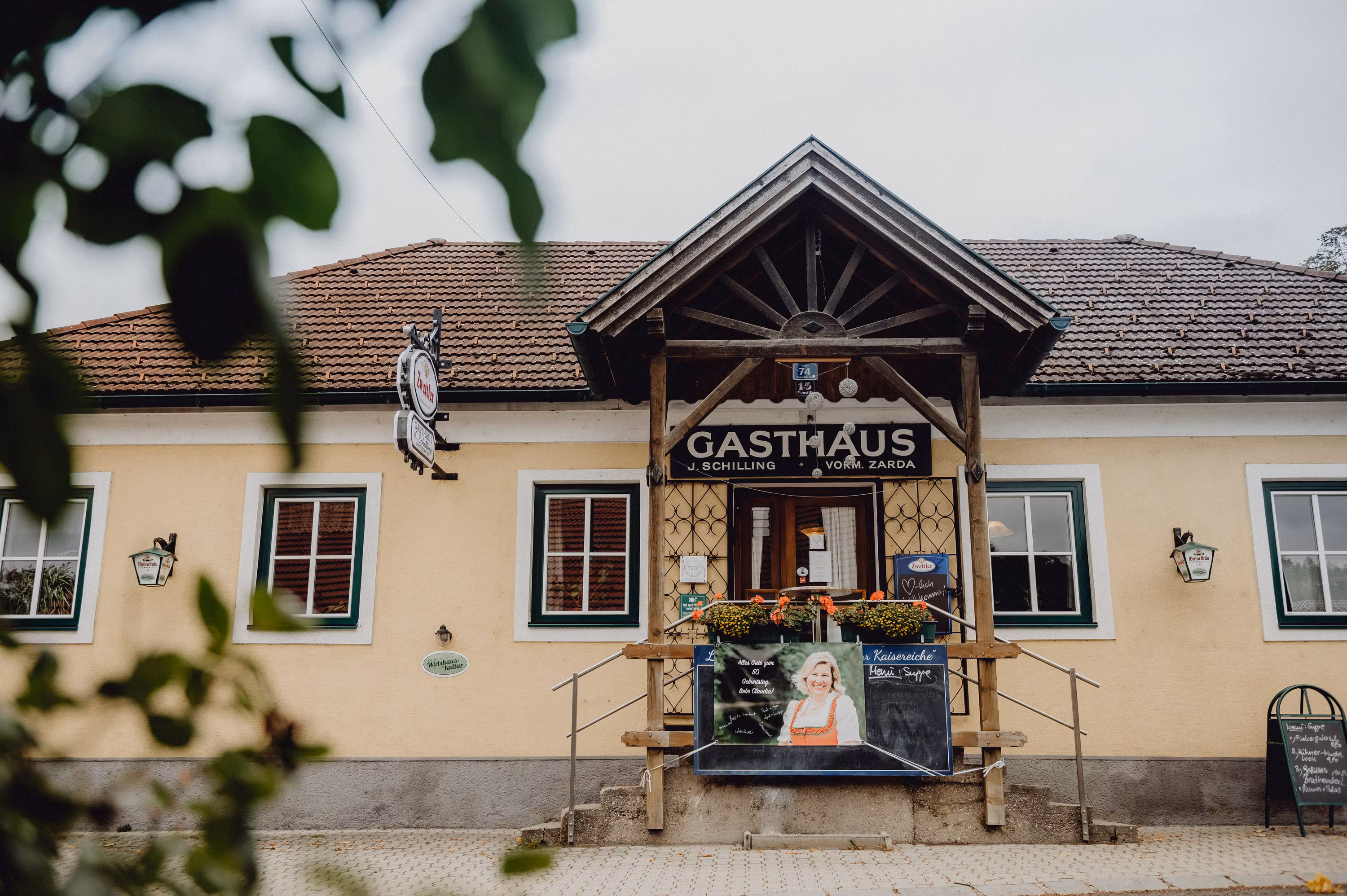 Eingang eines traditionellen Gasthauses mit Holzveranda und Werbetafel.