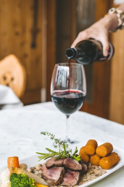 Fleischgericht mit Kroketten und Rotwein auf wei&szlig;em Tisch.