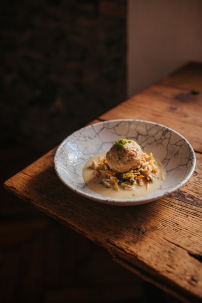 Ein Teller mit Gem&uuml;se Beuschel und einem Semmelkn&ouml;del auf einem Holztisch.