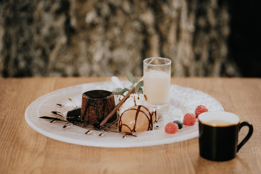 Ein Dessertteller mit Schokoladenkuchen, Eis, Beeren und einem Espresso auf einem Holztisch.
