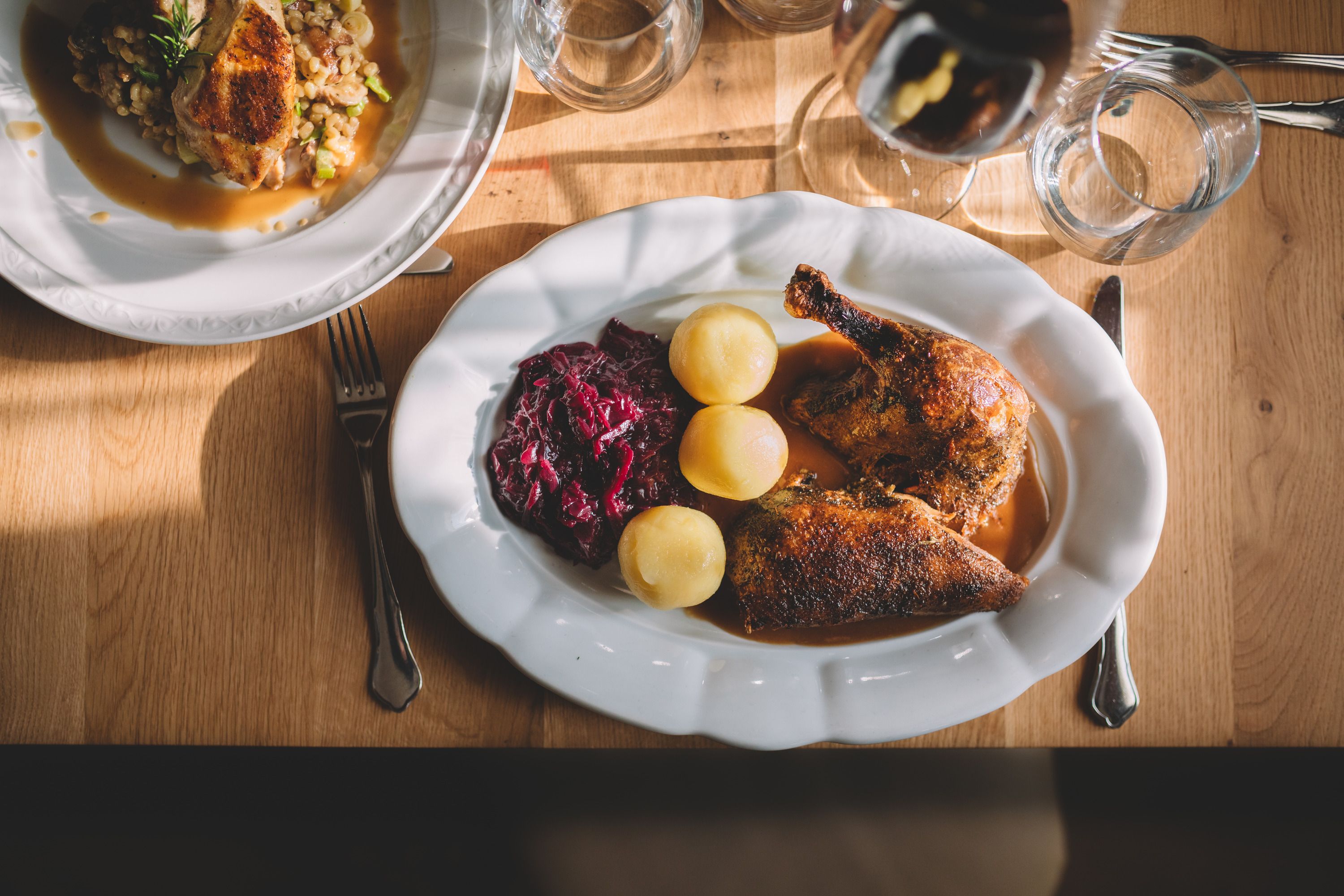 Ein Teller mit gebratener Ente, Rotkohl und Kartoffeln auf einem Holztisch.