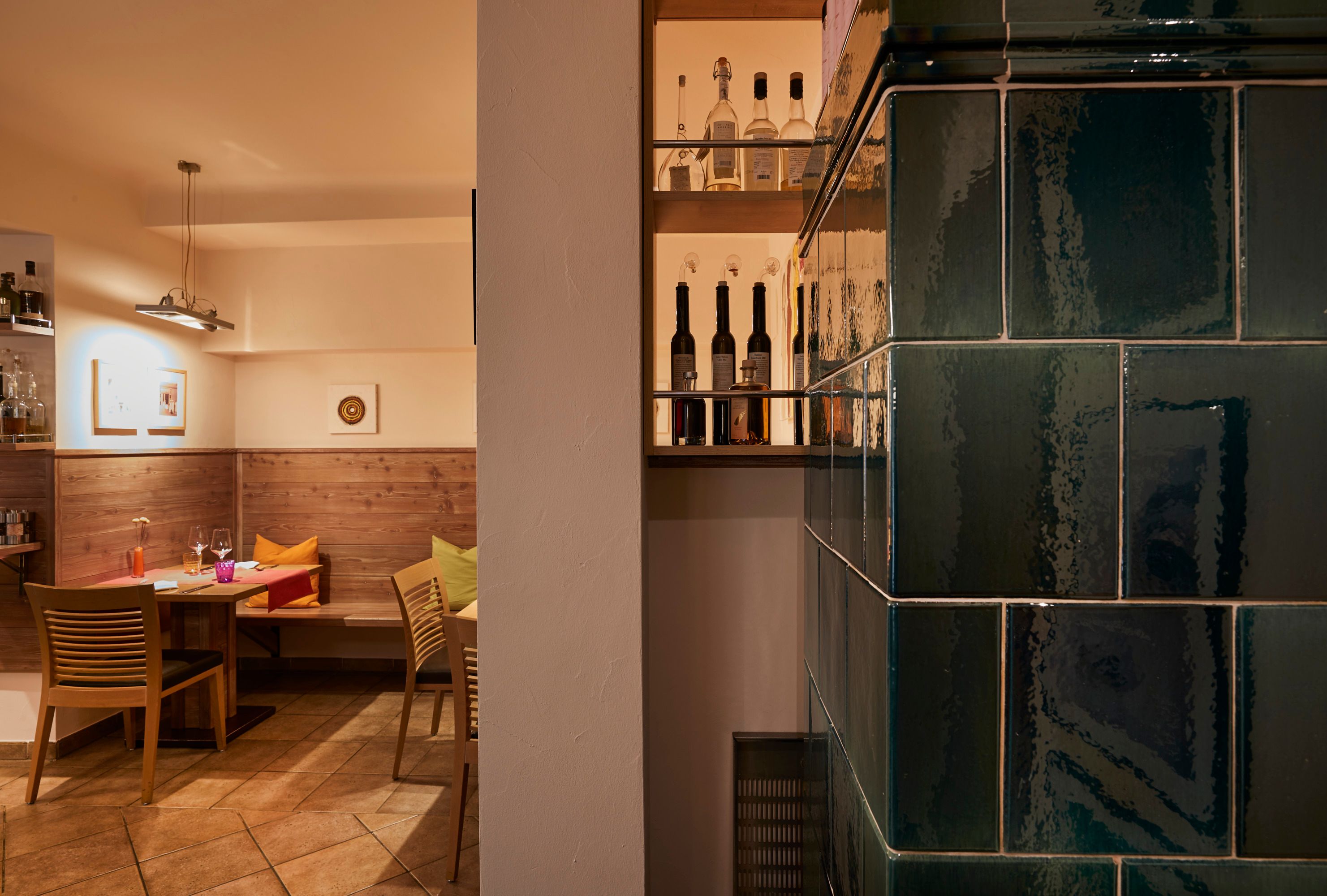 Gemütliche Stube mit Holzmöbeln, Kachelofen und Flaschenregal.