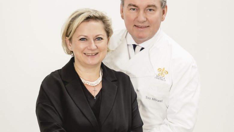 Ein Mann und eine Frau posieren lächelnd vor einem weißen Hintergrund.