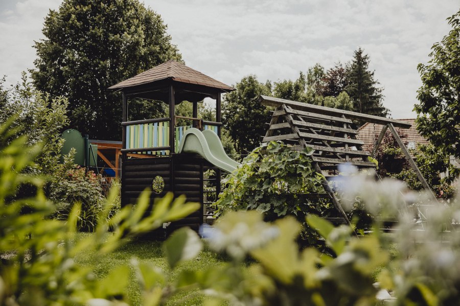 Ein Spielplatz mit Rutsche und Kletterger&uuml;st in einem gr&uuml;nen Garten.