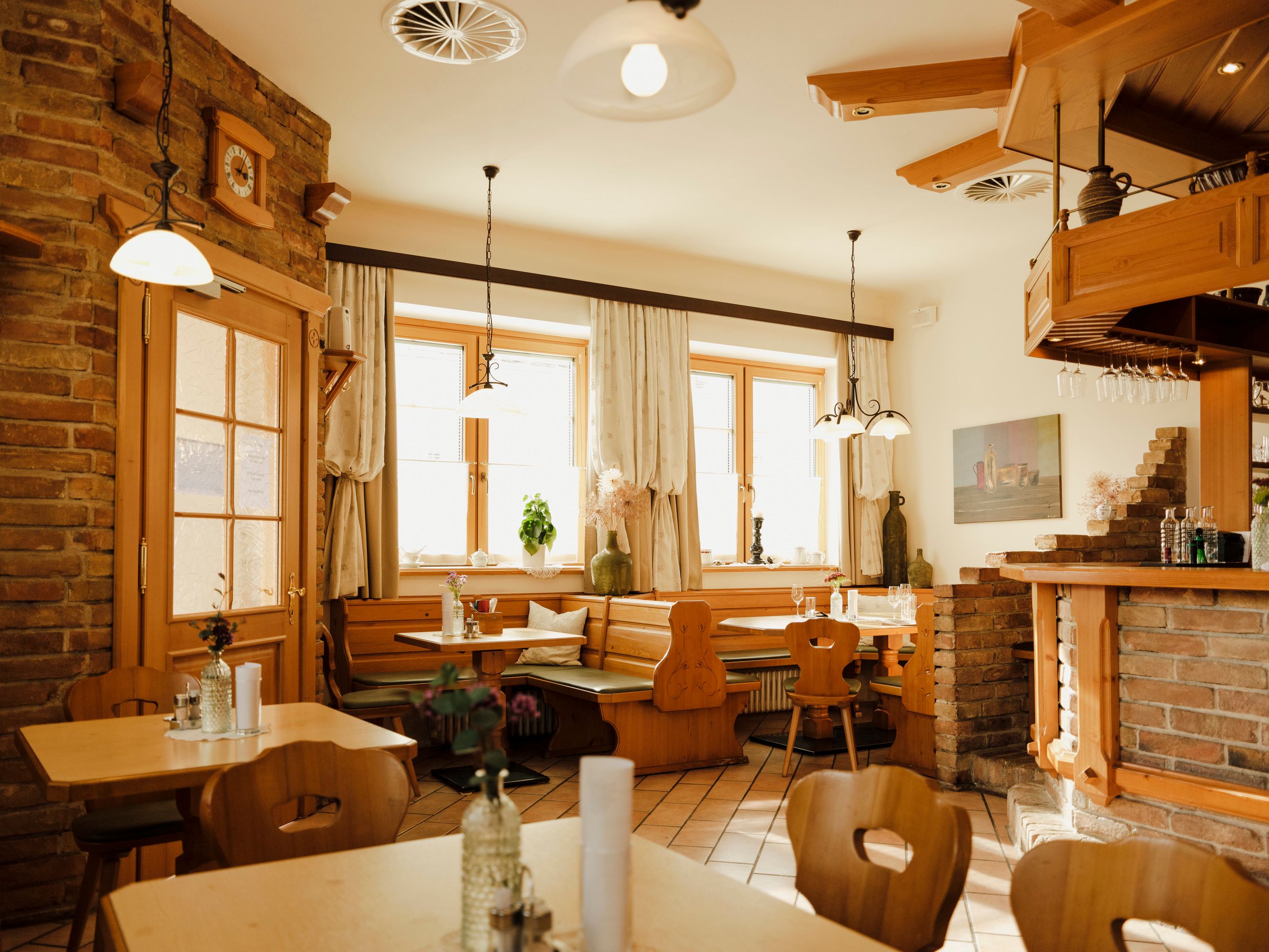 Gemütliche Gaststube mit Holzmöbeln und Backsteinwänden, dekoriert mit Pflanzen und Lampen.
