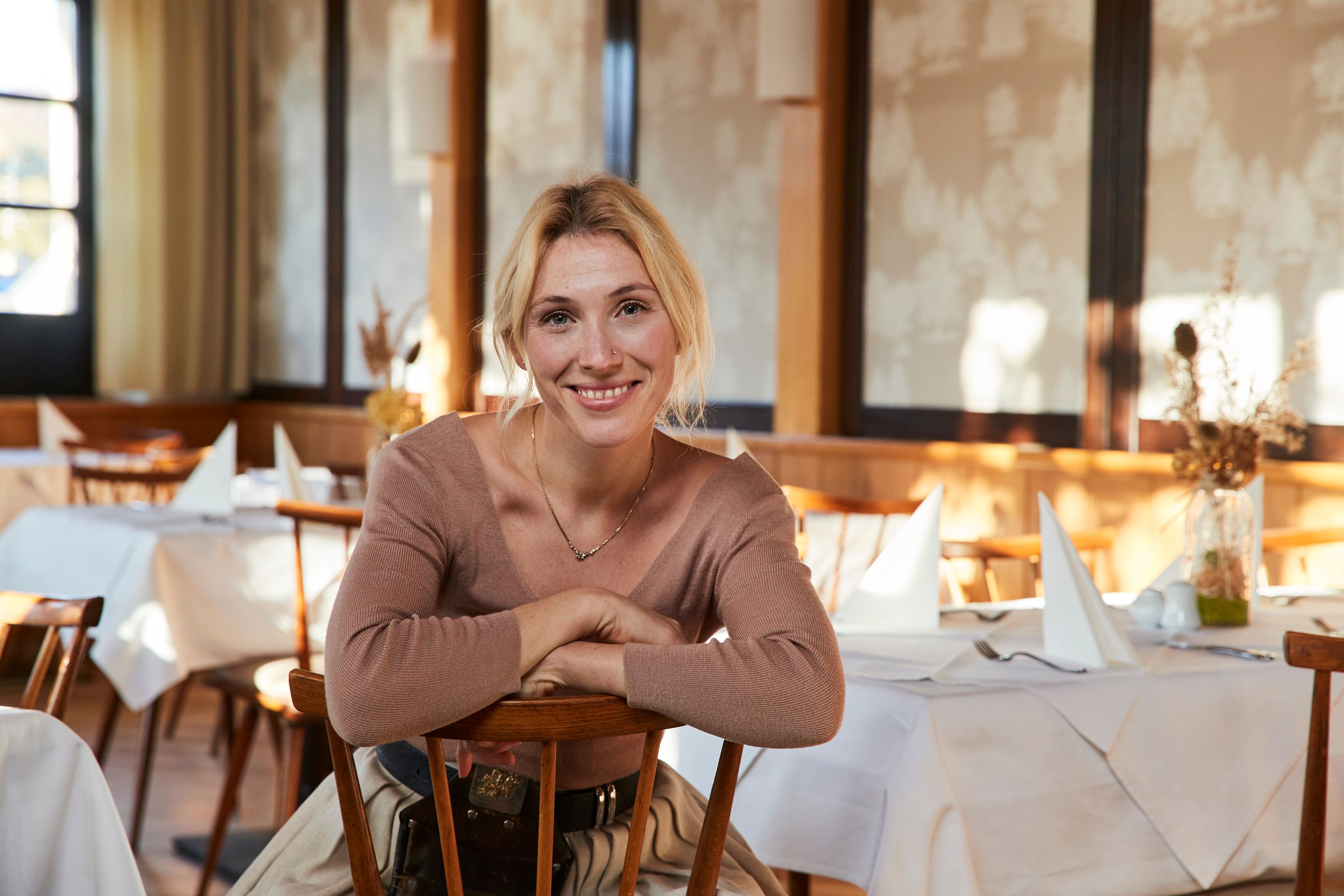 Frau sitzt lächelnd in einem Restaurant mit gedeckten Tischen.