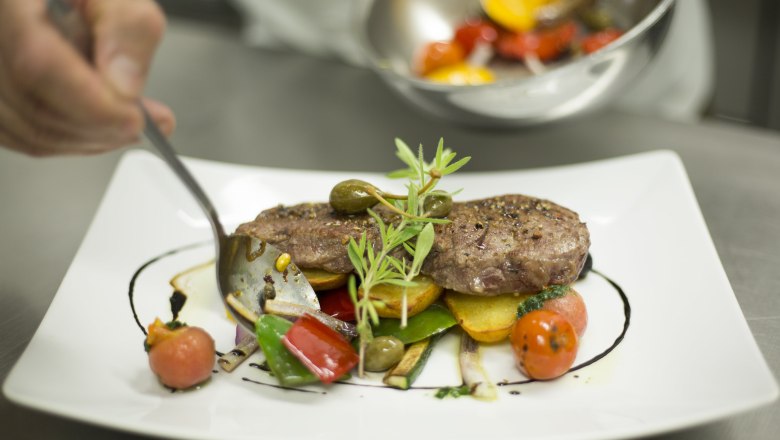 Ein Teller mit kunstvoll angerichtetem Fleisch, Gem&uuml;se und Kr&auml;utern.