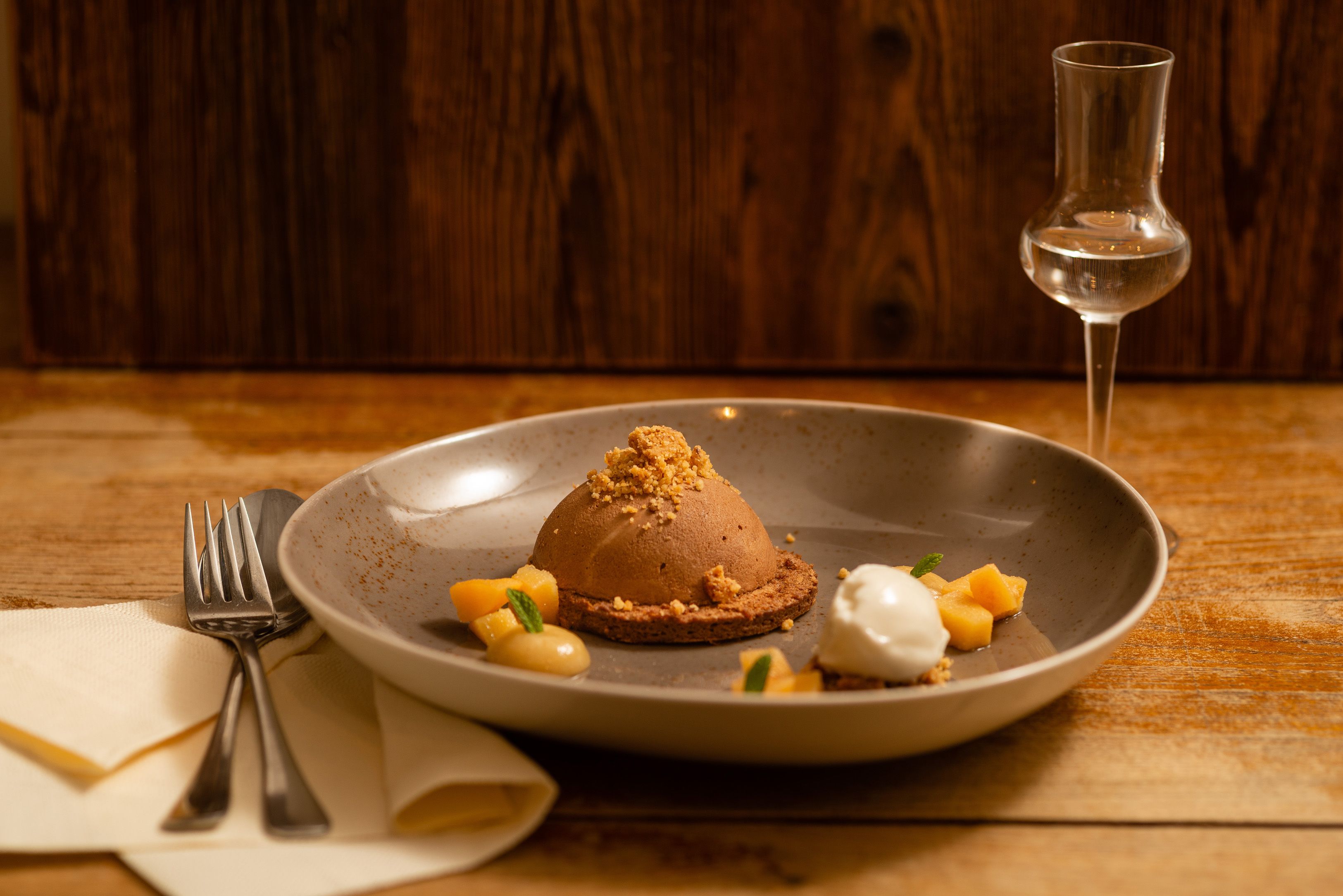 Schokoladendessert mit Keksboden, garniert mit Fruchtstücken und einem Klecks Sahne, daneben ein Glas Likör