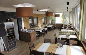 Innenansicht eines Wintergartens mit Tischen und St&uuml;hlen, gro&szlig;en Fenstern und moderner Dekoration.