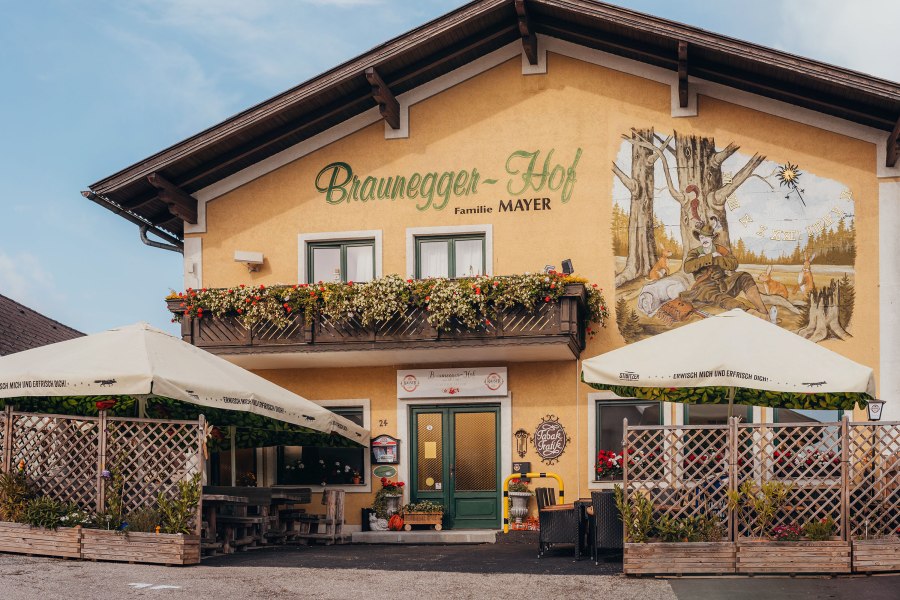 Ein traditionelles Gasthaus mit Balkon und Wandgem&auml;lde, umgeben von Sonnenschirmen und Pflanzen.