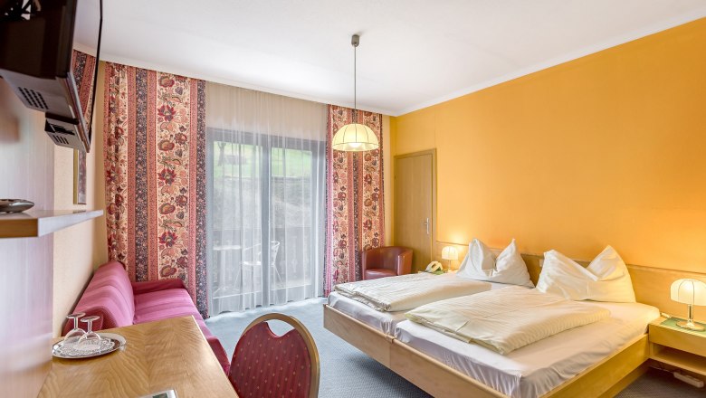 Hotelzimmer mit Doppelbett, gelben W&auml;nden, rotem Sofa und Balkon.
