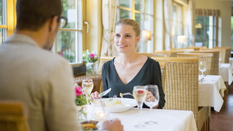 Ein Paar beim Abendessen in einem gem&uuml;tlichen Restaurant mit gro&szlig;en Fenstern und Kerzenlicht.