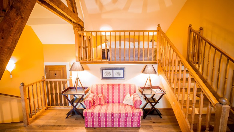 Gem&uuml;tliche Suite mit Holzbalken, Treppe, Sofa und Lampen.