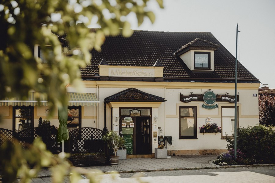 Traditionelles Gasthaus mit Schildern und Pflanzen im Vordergrund.