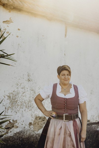 Frau in traditioneller Tracht vor einer alten Mauer.