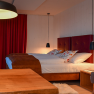 Gem&uuml;tliches Hotelzimmer mit Doppelbett, rotem Vorhang und Holzm&ouml;beln.