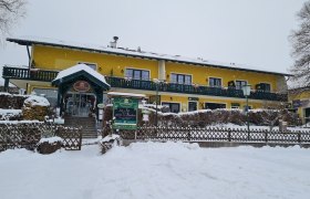 Gelbes Geb&auml;ude im Schnee mit gr&uuml;ner Veranda und Eingang.
