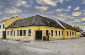 Gelbes Gasthaus an Stra&szlig;enecke mit bew&ouml;lktem Himmel im Hintergrund.