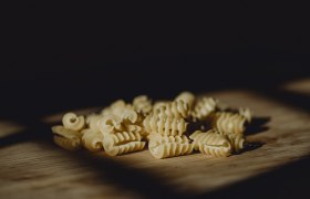 Nahaufnahme von ungekochten, spiralförmigen Nudeln auf Holzuntergrund.