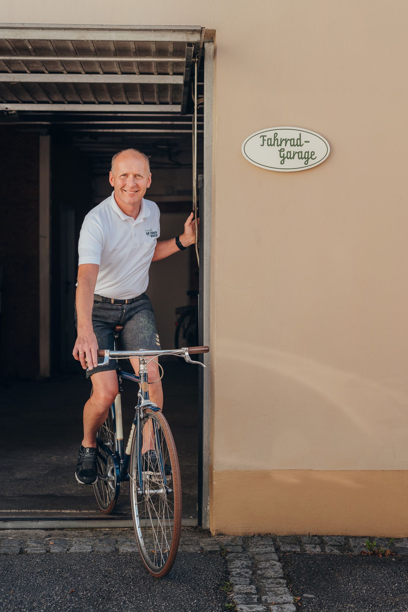 Mann fährt Fahrrad aus einer Garage mit Schild 'Fahrrad-Garage'.