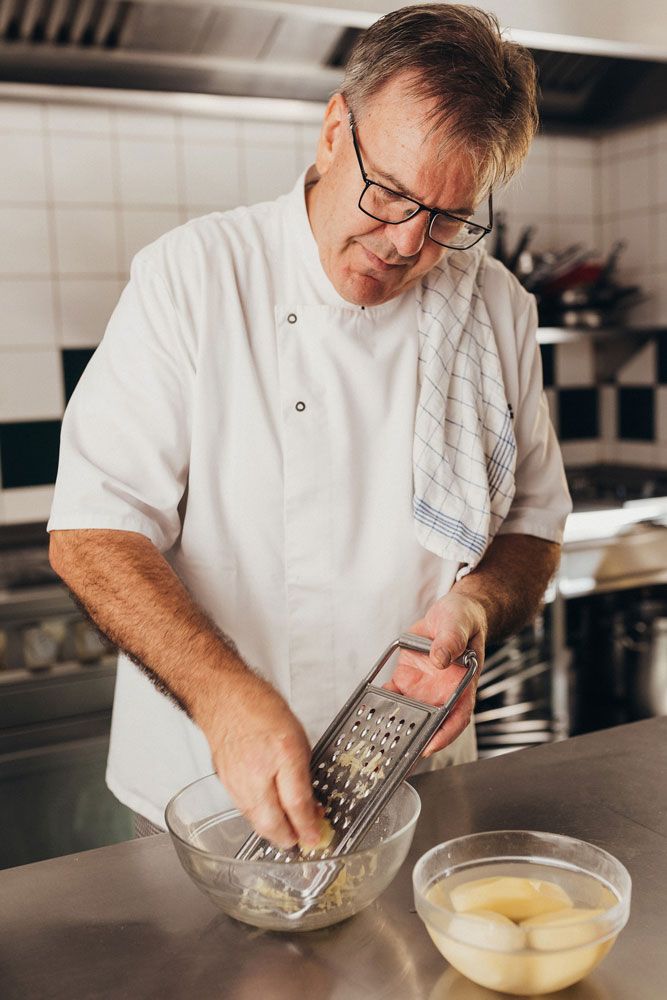 A cook grates potatoes in a kitchen.