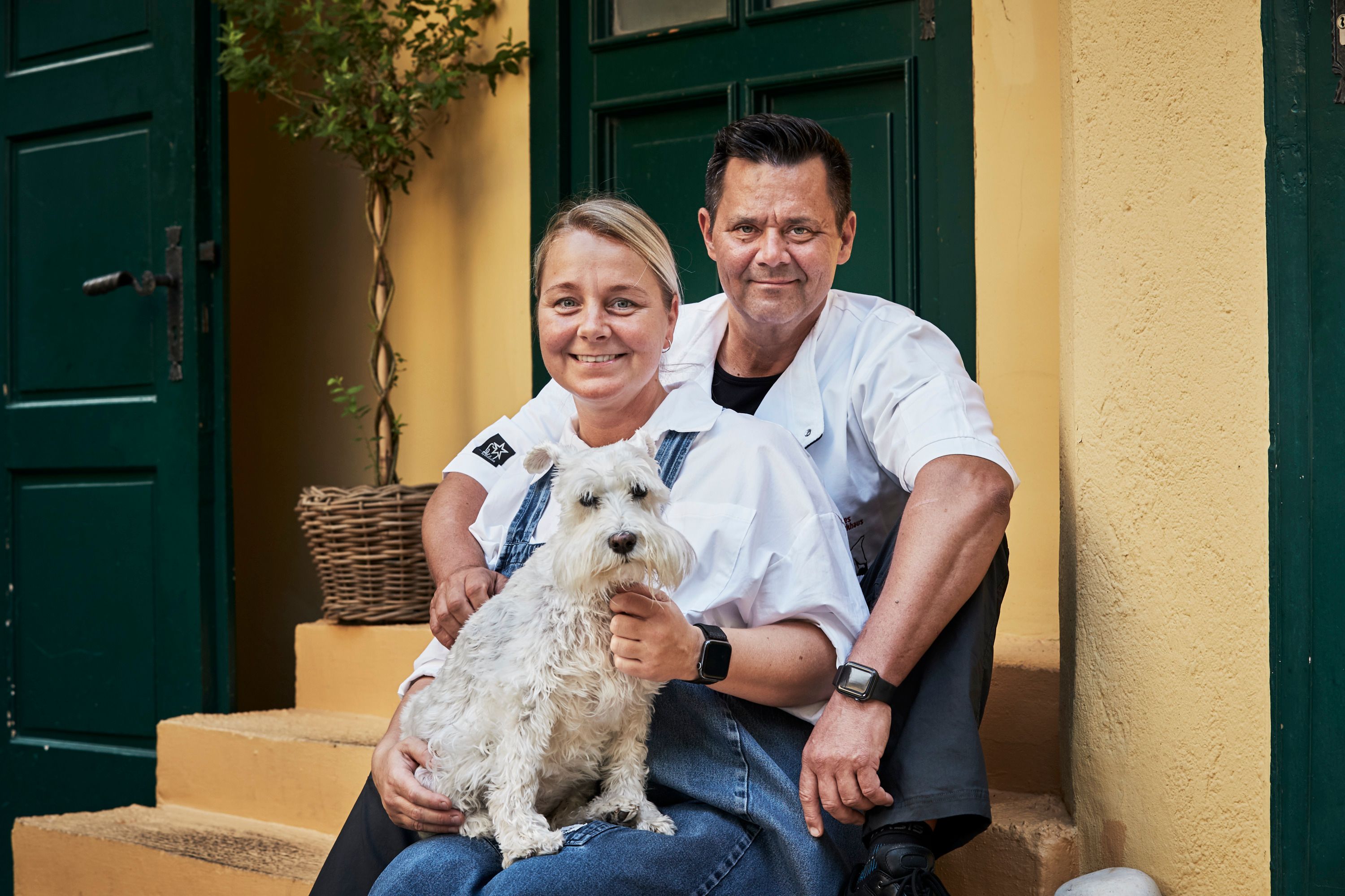 Ein Mann und eine Frau sitzen auf einer Treppe mit einem kleinen weißen Hund.