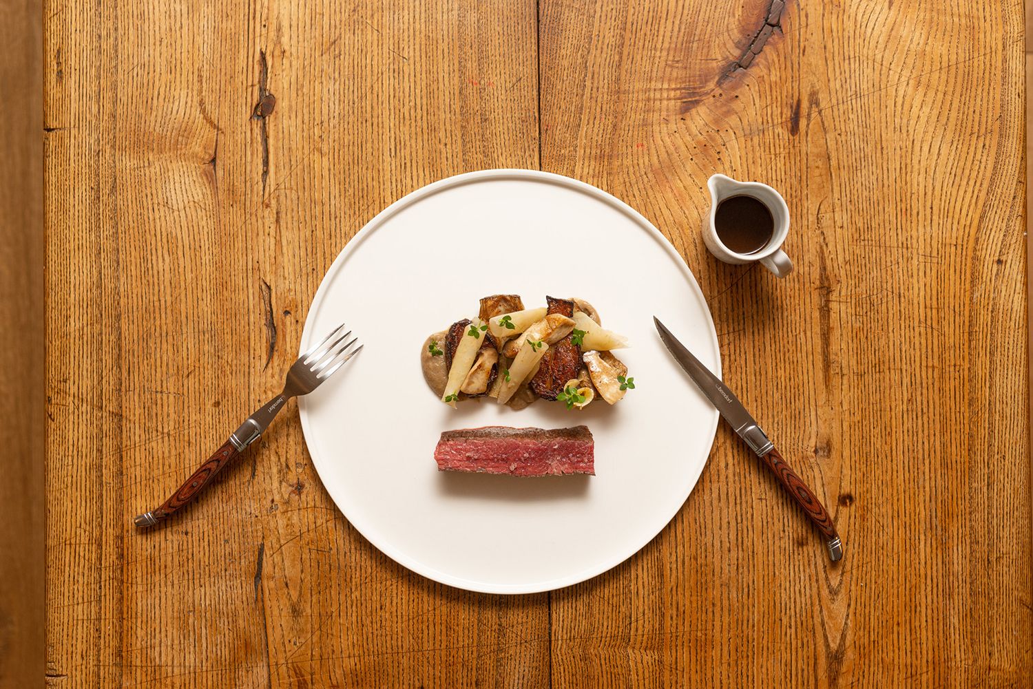 Ein Teller mit Beiried, Artischocken, Kräuterseitlingen und Topinambur auf einem Holztisch.