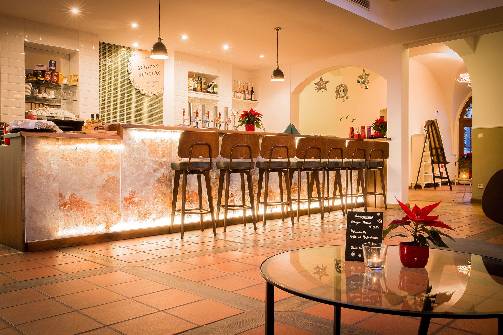 Elegante Bar mit beleuchtetem Tresen und hohen Stühlen, dekoriert mit Weihnachtssternen.