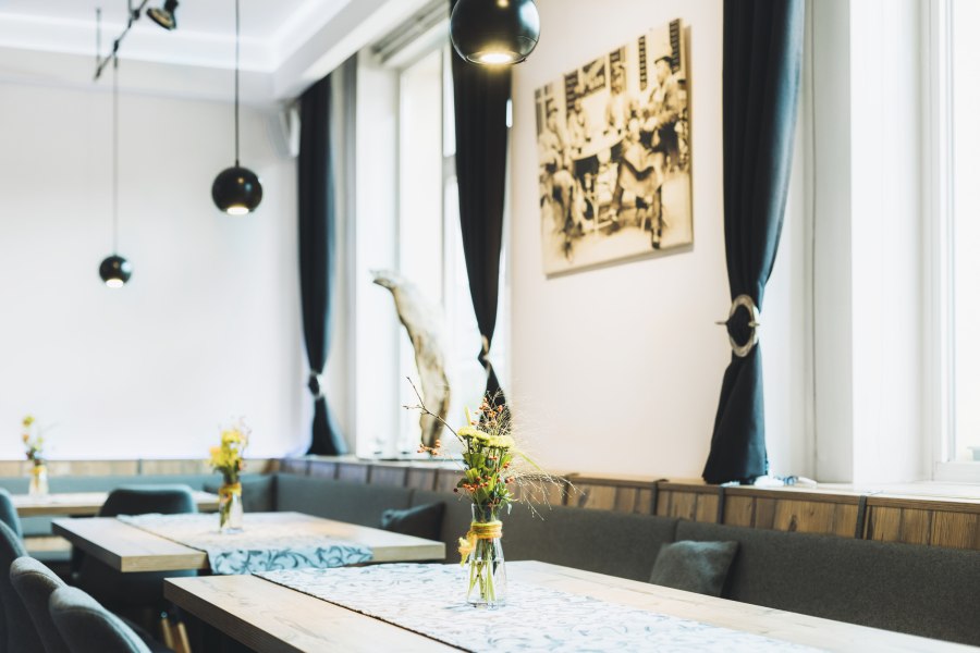 Innenansicht eines stilvollen Caf&eacute;s mit Holztischen, Blumenvasen und schwarzen Vorh&auml;ngen.