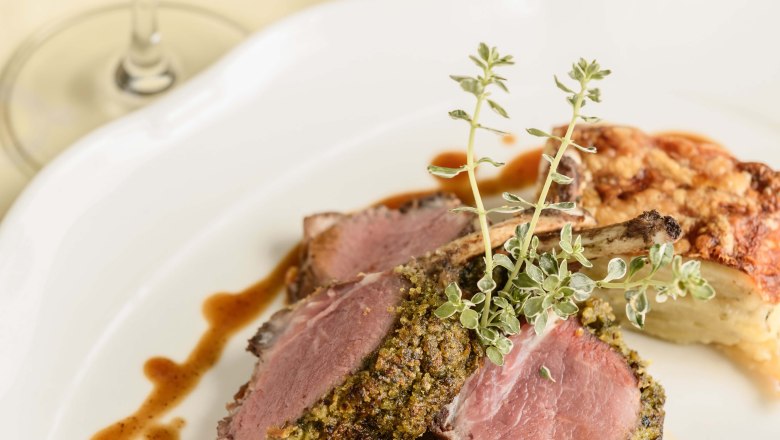 Ein Teller mit Lammkoteletts in Kräuterkruste, Gemüsebeilage und Soße, daneben ein Glas Rotwein.