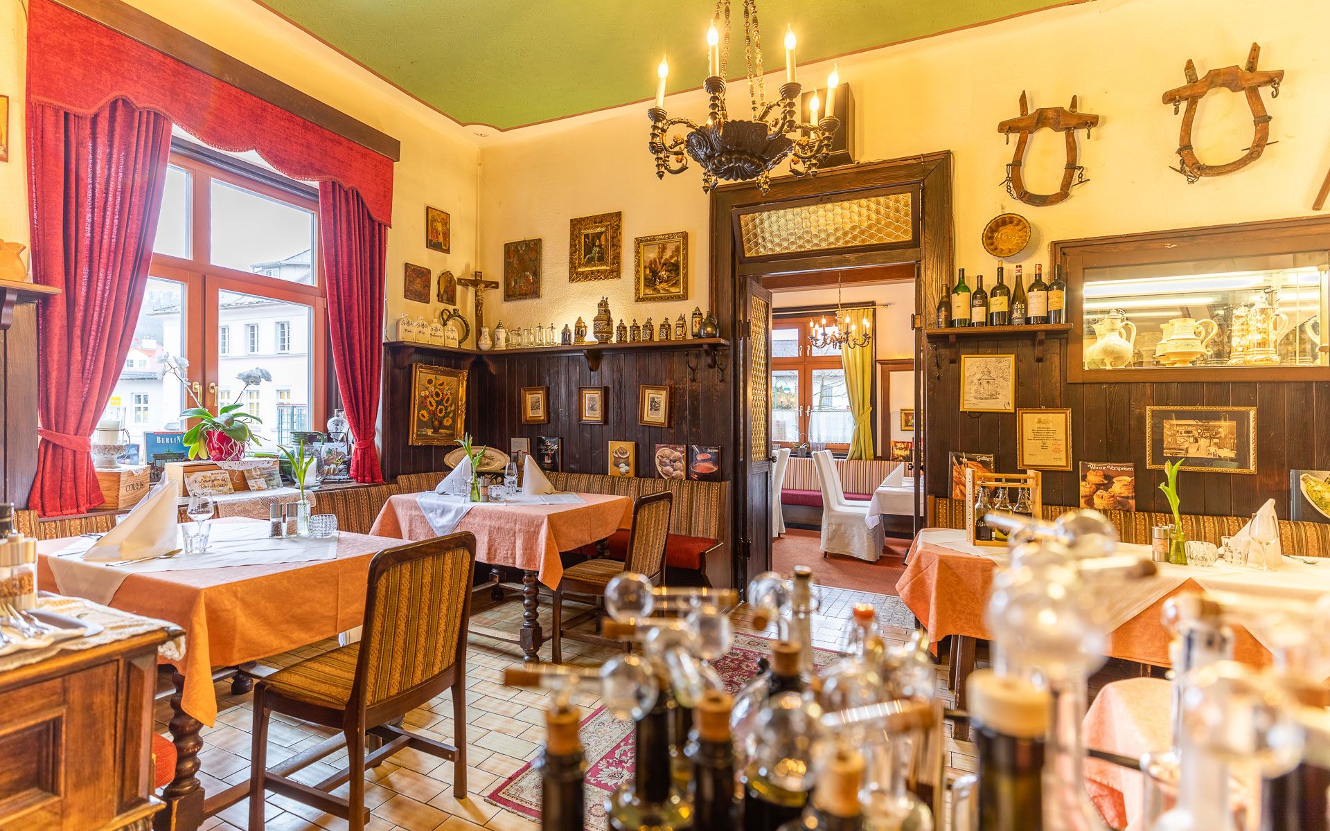 Gemütliches Restaurant mit Holzmöbeln, roten Vorhängen und dekorativen Bildern an den Wänden.
