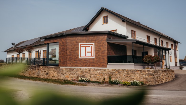 Ein modernes Geb&auml;ude mit der Aufschrift 'Gasthof Thaler', umgeben von einer Steinmauer und Pflanzen.