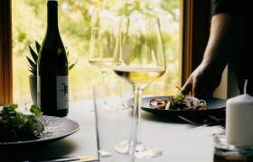 Ein gedeckter Tisch mit Weinflasche, Weingl&auml;sern und einem Teller mit Essen in einem Restaurant.