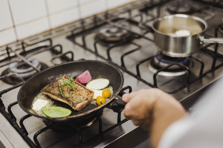 Eine Pfanne mit Fisch, Gem&uuml;se und Kr&auml;utern auf einem Herd.