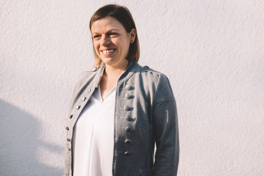 Frau in grauer Jacke vor weißer Wand.