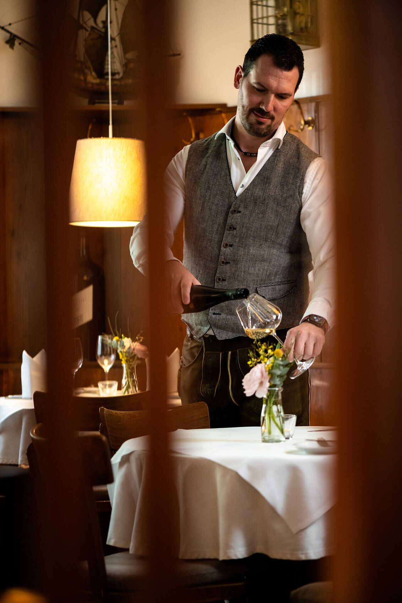 In der gemütlichen Gaststube des Dreikönigshofs wird eine einladende Atmosphäre geschaffen, während der Wirt mit einem eleganten Service das köstliche Getränk einschenkt. Die liebevoll dekorierten Tische und die sanfte Beleuchtung laden dazu ein, die regionale Wirtshauskultur in vollen Zügen zu genießen.