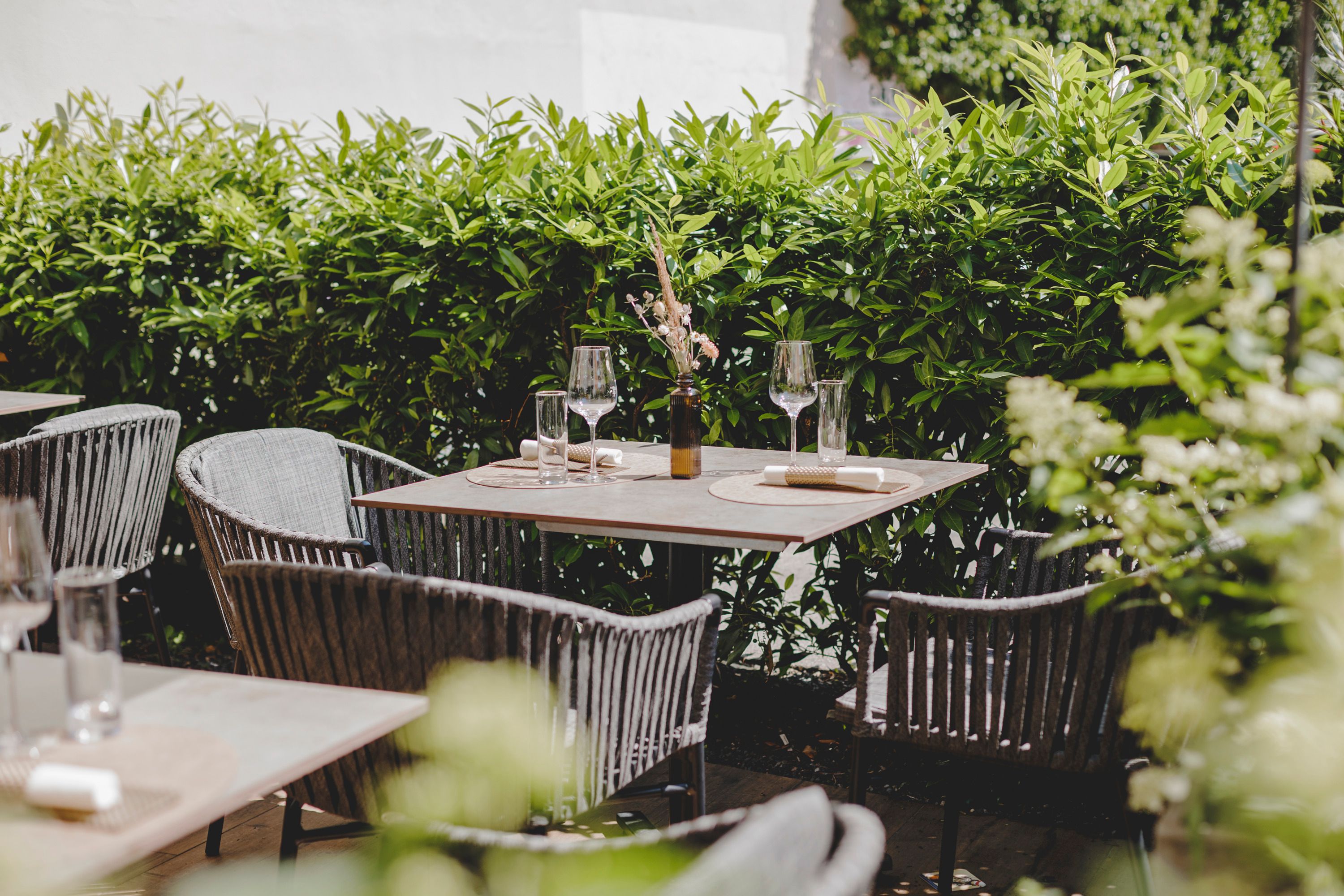 Ein gemütlicher Gastgarten mit gedeckten Tischen und grüner Hecke im Hintergrund.